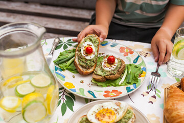 Rustic avocado toasts on oval bread served for a cozy family brunch with orange juice, croissants,...