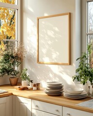 Bright sunlight streams into a modern kitchen, illuminating a light wood countertop with stacked dishes and potted plants. A large, light wood framed picture sits on the wall. 
