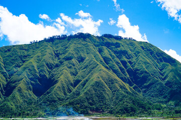 Panoramic view of green landscape with mountains, blue sky and white clouds from Selong Hill, Sembalun, Lombok, West Nusa Tenggara, Indonesia.