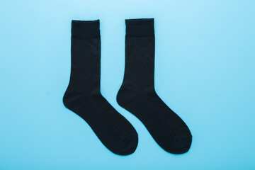 Two new dark black long male socks on light blue table background. Pastel color. Closeup. Top down view.
