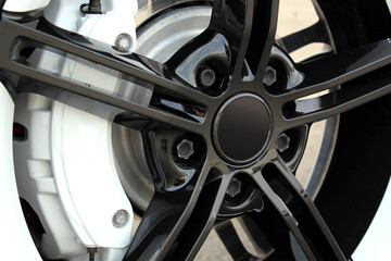 Close-up Black and white front wheel of sports car. Huge alloy wheel of sports car with diameter 21 inches. Huge brake disc and caliper of sports car.