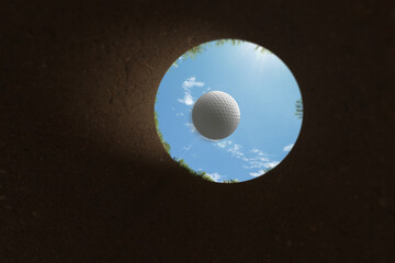 Golf ball falling into the hole from inside the cup view