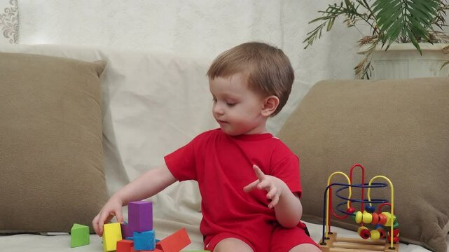 Happy baby play educational toys. Portrait of a smiling child playing while sitting on the sofa. Kid about one two years old. baby at home playing with toys