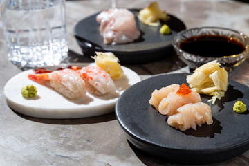 Delicately crafted sushi pieces, including shrimp and white fish, lie artfully arranged on stylish plates. Vibrant wasabi and pickled ginger accompany the meal, enhancing the culinary experience