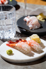 Delight in a carefully arranged sushi platter featuring succulent shrimp, vibrant wasabi, and pickled ginger. This gourmet experience is complemented by crystal-clear water, set in a stylish eatery