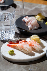Exquisite sushi platter showcases fresh shrimp, elegant slices of fish, wasabi, and ginger, set against a stylish table. A glass of water complements the culinary experience in bright light