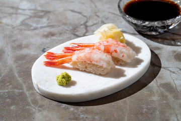 Elegant sushi creation features plump shrimp nigiri artfully arranged on a sleek marble plate, accompanied by zesty wasabi and pickled ginger, perfect for a gourmet experience