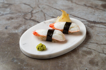 A beautifully arranged sushi platter features three pieces of nigiri with shrimp and a touch of seaweed. Accompanied by wasabi and pickled ginger, it's a culinary delight
