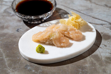 Savor the artistry of seafood with finely crafted shrimp sushi, accompanied by a touch of wasabi and pickled ginger, creating a perfect balance of flavors on a textured surface