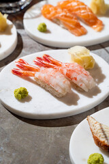 An exquisite assortment of sushi showcases succulent shrimp on white plates, accompanied by a touch of vibrant wasabi and soft ginger. A luxurious dining experience awaits