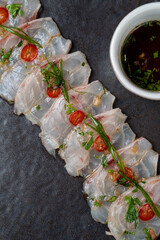 Delicate slices of sashimi arranged artistically on a dark plate, garnished with fresh herbs and...