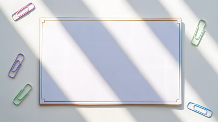 Blank notepad with gold border and colorful paper clips on white desk with soft diagonal shadows in sunlight