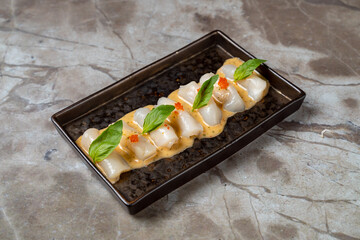 Delicately arranged sashimi showcases fresh fish topped with vibrant chili sauce and herbs, served on a sleek black plate against a muted backdrop, reflecting culinary artistry in a stylish eatery