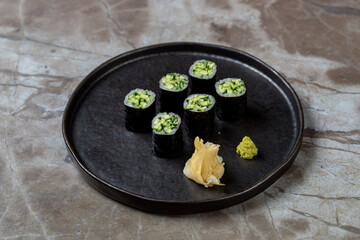 Delicate sushi rolls filled with crisp cucumber are elegantly displayed on a dark ceramic plate, accompanied by a side of pickled ginger and a dollop of vibrant wasabi