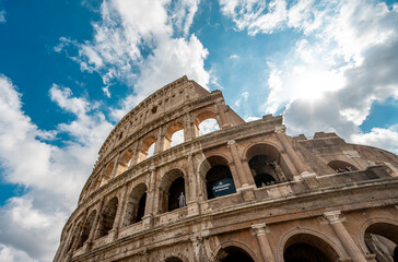 Fototapeta premium A bright blue and sunburst sky with clouds over the Roman Colosseum in Rome, Italy