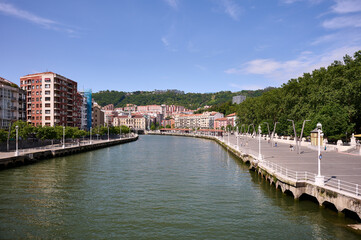 Obraz premium Scenic view of Nervion river, residential buildings, and promenade in Bilbao, spain, on a sunny summer day