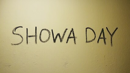 Black handwritten text 'SHOWA DAY' on a beige wall, representing a holiday name.