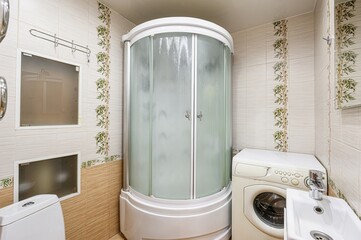 bathroom interior featuring a shower cabin, toilet, washing machine, and sink. The walls are tiled...