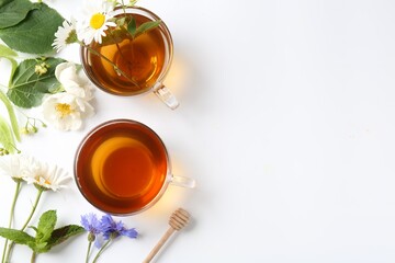 Aromatic herbal tea in glass cups, different flowers and green leaves on white background, flat lay. Space for text