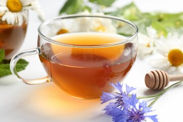 Aromatic herbal tea in glass cup, different flowers and dipper on white background, closeup