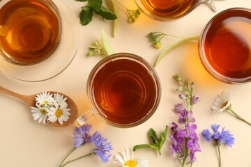 Aromatic herbal tea in glass cups and different flowers on beige background, flat lay