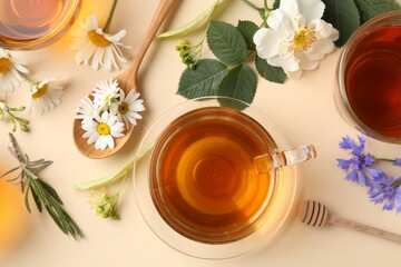 Aromatic herbal tea in glass cups and different flowers on beige background, flat lay