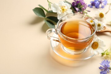 Aromatic herbal tea in glass cup and different flowers on beige background, closeup. Space for text