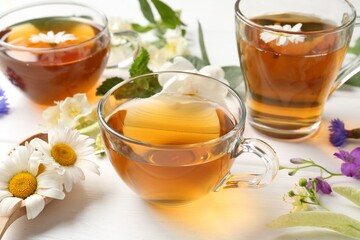 Aromatic herbal tea in glass cups and different flowers on white wooden table, closeup
