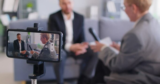Male guest gives interview to female reporter during phone video recording or live broadcast for tv show, focusing on news and pr in a professional setting with engagement and visibility.