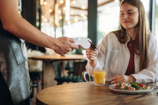 Waiter is holding terminal. Woman is paying for meal by wireless payment in the cafe restaurant
