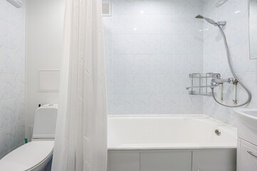 bright bathroom featuring a white bathtub with a shower head, a white toilet behind a shower curtain, and blue-tiled walls