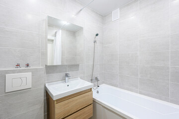 well-lit, modern bathroom featuring gray tiles, a wooden sink cabinet, a white bathtub, and a mirror