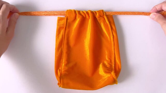 Asian woman's hands closing yellow velvet drawstring pouch on white tabletop background. Drawstring bag for make merit. Homemade. Bangkok, Thailand./ Slow down video