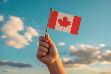 Vibrant sunlit portrait capturing a hand holding a small Canadian flag proudly against a dynamic sky with soft, scattered clouds