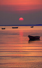 Serene sunset over calm water with silhouetted boats at golden hour