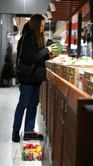 Young woman choosing cabbage in vegetable section of supermarket