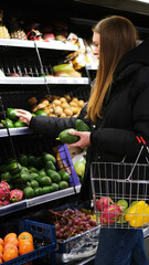 Young caucasian woman choosing zucchini and broccoli in supermarket