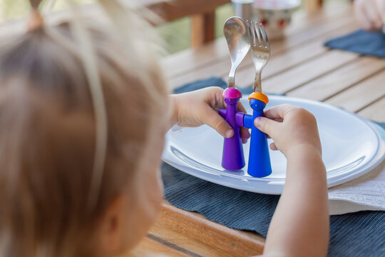 Young child interacts with colorful utensils, engaging in imaginative play at a wooden table during a family gathering