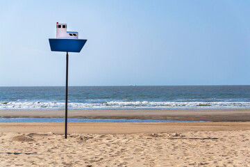 Wooden model of a blue and white boat on pole on a sandy beach, coastal village De Haan, West Flanders, Belgium