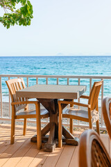 Coastal dining area with wooden chairs overlooking clear blue ocean on a bright sunny day