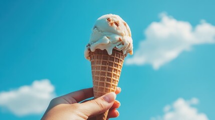 Hand holds a waffle cone with melting ice cream against a vibrant sky. Use it for summer promotions, food blogs, or a sweet treat concept.