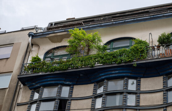 Ornate residential building facade with curved balcony, green plants, and arched windows 