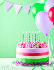 A festive three-layer birthday cake with pink, green, and white frosting is adorned with lit candles, colorful sprinkles, and vibrant balloons against a light green background