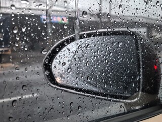 Raindrops on car window with blurred side mirror view