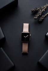 Smartwatch with Rose Gold Band: Elegant smartwatch with a rose gold band rests on a dark surface, surrounded by black gift boxes and a sprig of lavender.