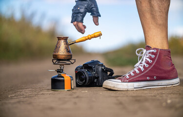 Obraz premium Photographing Turkish coffee maker on field road. Camera and male leg and hand. Concept of travel and adventure outdoors.
