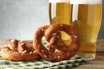 Tasty pretzels and glasses of beer on wooden table against grey background, closeup