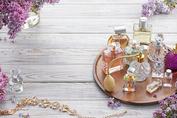 Bottles of perfumes, accessories and lilac flowers on white wooden table. Space for text