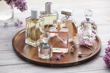 Bottles of perfumes and lilac flowers on white wooden table, closeup