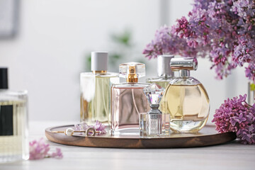 Bottles of perfumes and lilac flowers on white wooden table